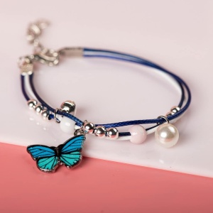 Armband med blå fjärilshänge med vita pärlor mot en vit och rosa bakgrund