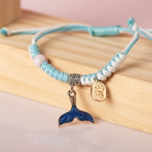 Flätat armband med hängsmycke av havsdjur i blått och vitt, på en trähylla