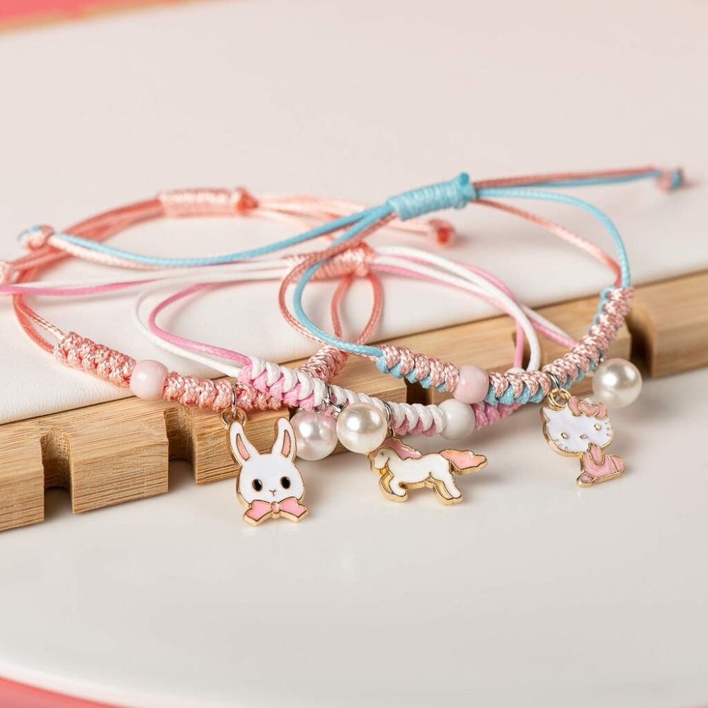 Vävt armband med pärlhänge och rosa och blått djur mot en vit och träbakgrund