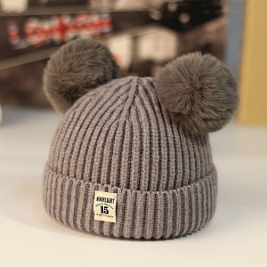 Stickad mössa med dubbel brun pompon på ett bord
