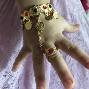 Armband och ring sammanlänkade med en kedja för en liten flicka på en barnhand med vit kjol