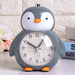 Multifunktionell väckarklocka i form av en grå, vit och orange pingvin på en vit hylla
