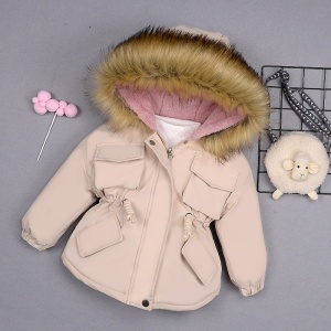 Enfärgad parkas med pälsluva i beige på en grå vägg med svart järnkorg