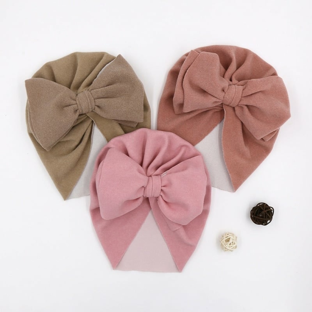 Barnturban med stor rosett Turban med stor rosett för barn, rosa och brun på ett vitt bord