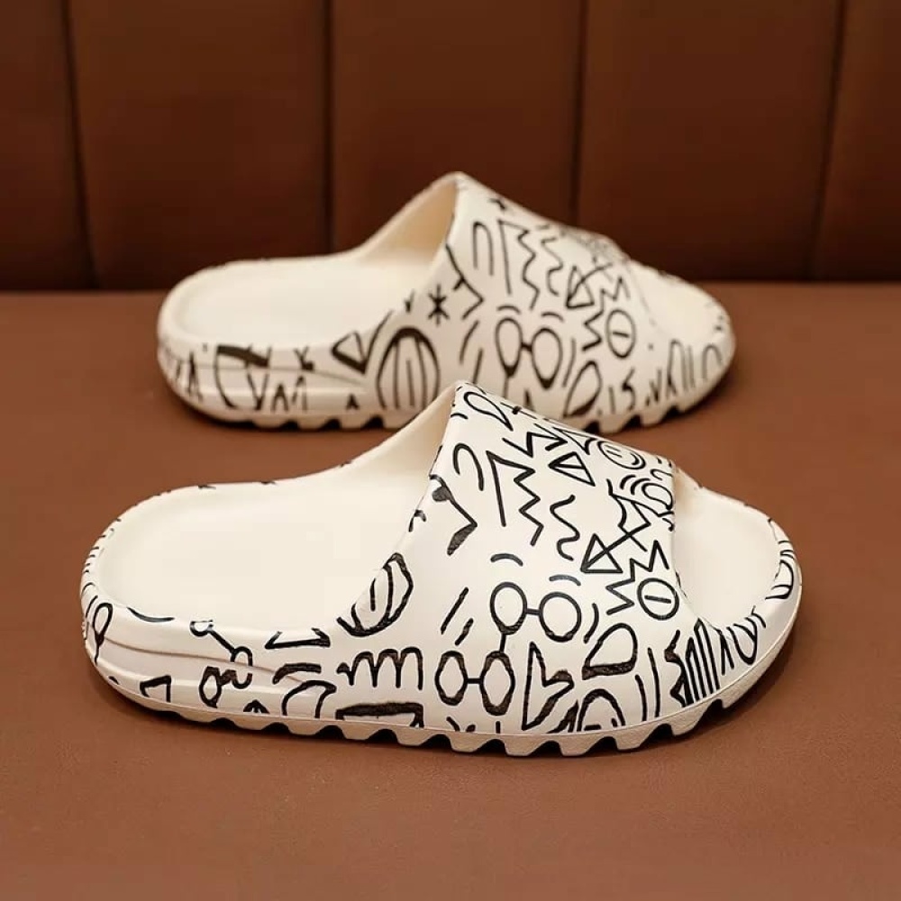 Bekväma sommarflip-flops för alla i vitt med svart em-mönster på en brun hylla