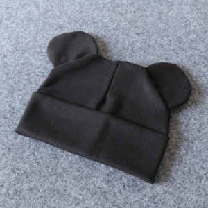 Babyhuv i bomull med små öron i svart mot en grå bakgrund