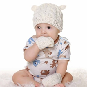 Vit vintermössa och vantar för baby med baby med handen i munnen och vita mönstrade kläder