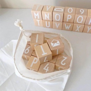Alfabetleksak i trä att stapla i en vit påse på ett vitt bord