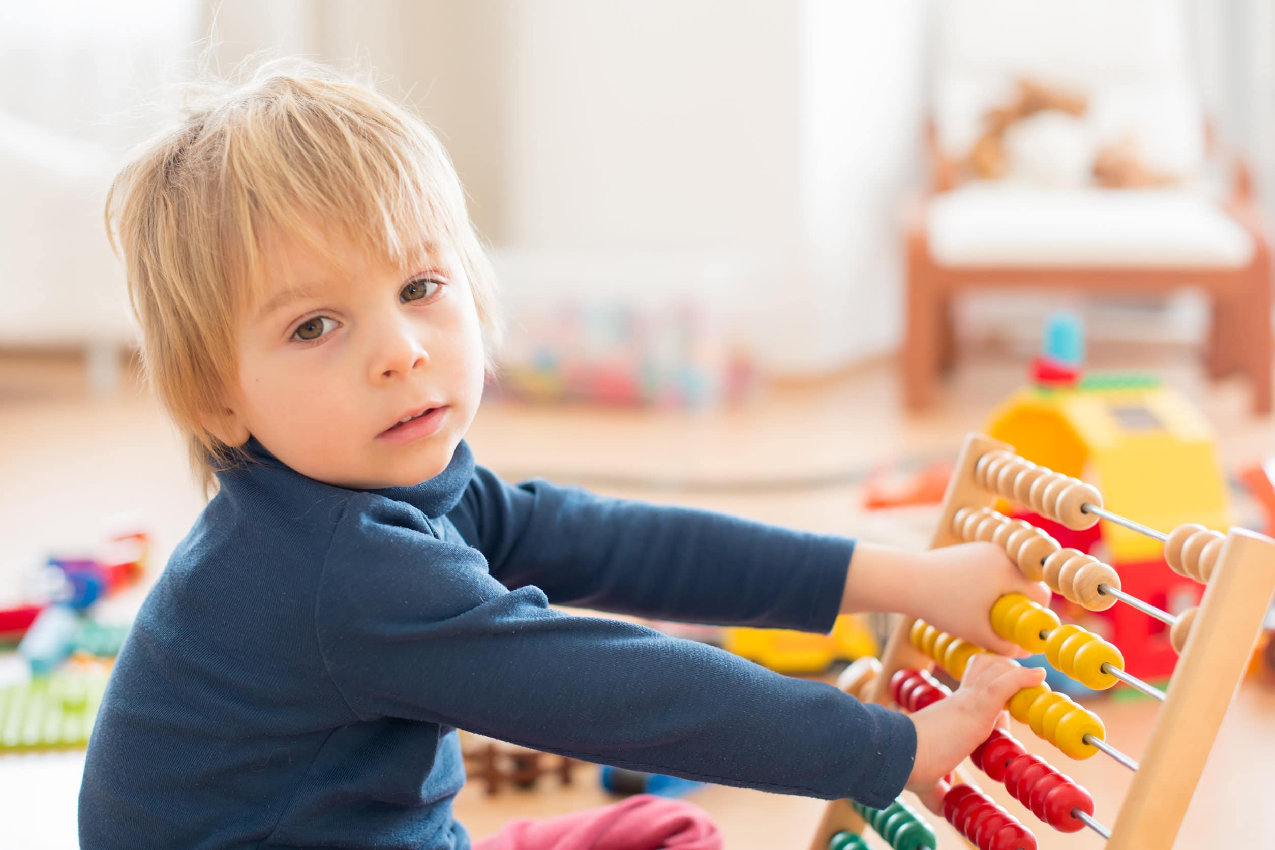 En ung pojke med medellångt blont hår och blå tröja leker med en färgad abakus för att lära sig räkna
