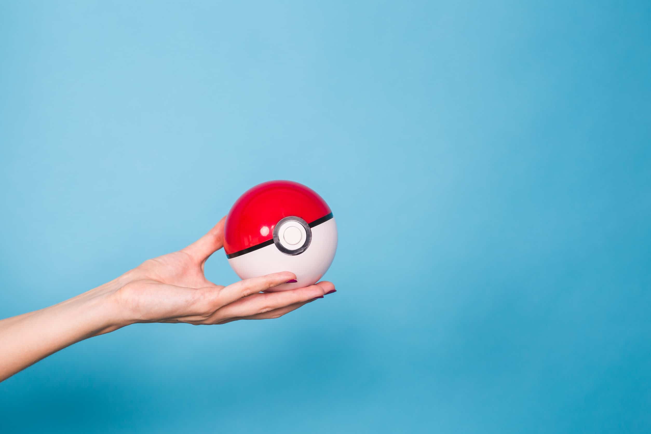 En hand som håller en röd och vit pokémon-pokeboll mot en blå bakgrund