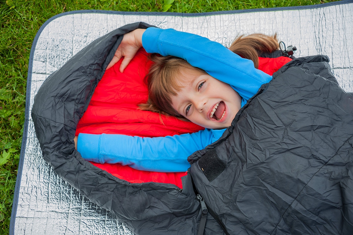En liten flicka ligger i sin grå sovsäck för barn