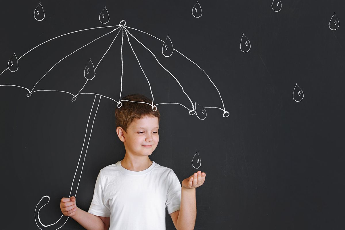 En ung pojke i vit T-shirt står framför en målning som föreställer ett paraply och regndroppar