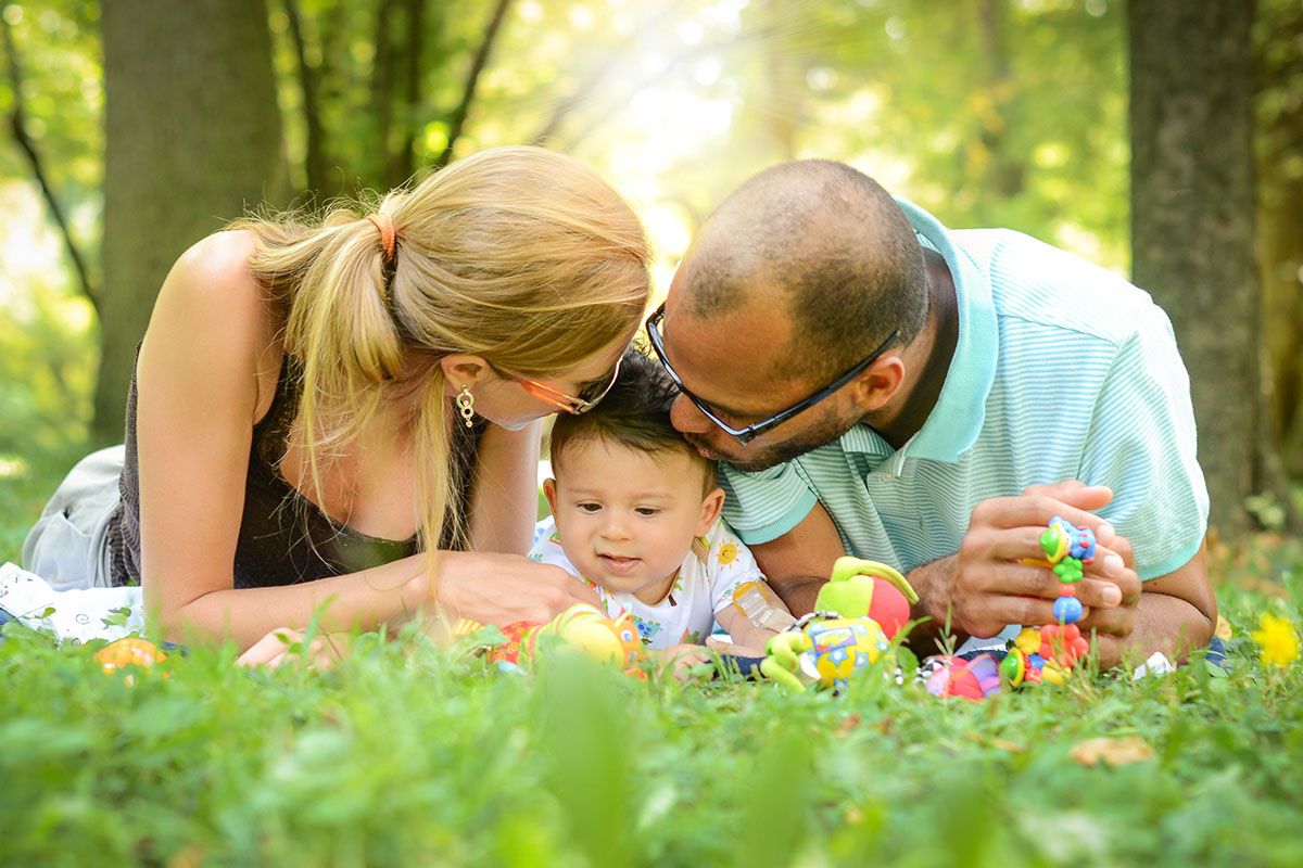 En lycklig familj ligger på gräset. I mitten finns mamma, pappa och deras bebis.