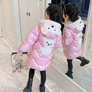Lång, blank jacka med luva och björn för flickor i rosa med björn i luvan och på ryggen på en flicka framför en spegel