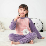 Pyjamas i flanellfleece med ett sött mönster för barn i lila och rosa på en flicka i en vit matta med en kudde i ryggen