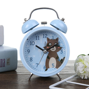 Blå väckarklocka för barn med motiv av en brun tvättbjörn, placerad på en brun möbel bredvid en vit blomma