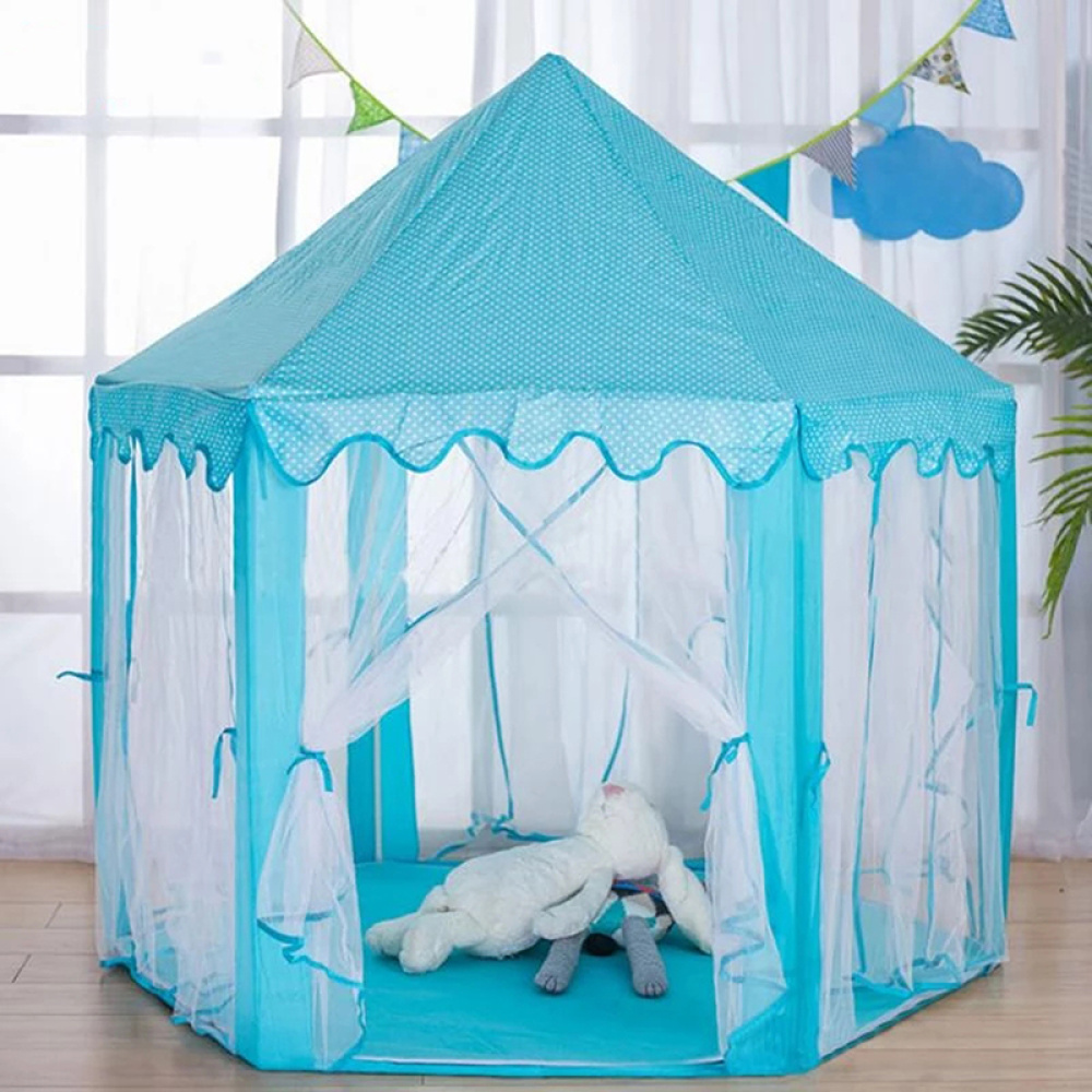 En barntipi i form av ett blått prinsesslott. Den står på golvet i ett vardagsrum, med ett stort fönster bakom. Alla väggar är gjorda av genomskinligt myggnät, och på framsidan är gardinerna i öppet läge, med gardinerna hängande längs stolparna.