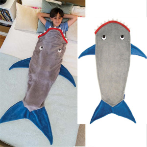 Bilden är uppdelad i två delar, den första visar ett barn som ligger i sängen, nedstoppat i en grå hajformad sovsäck med blå fenor och en röd mun. Den andra delen av bilden visar sovsäcken mot en vit bakgrund.