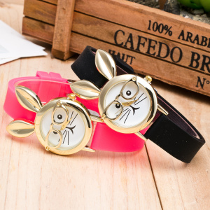 på ett träbord, två klockor av samma modell, nära en trälåda, en rosa och en svart, med en söt liten kanin med glasögon på urtavlan