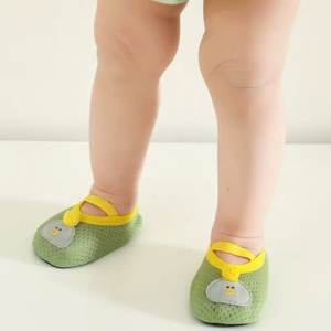 en baby står med bara benen synliga och bär små, mjuka, gröna tossor som andas