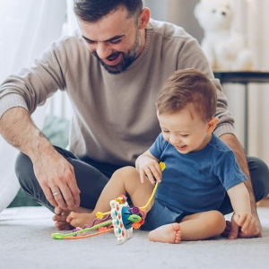 Montessori-tuggleksak i silikon för spädbarn med bakgrund av en pappa med sitt spädbarn