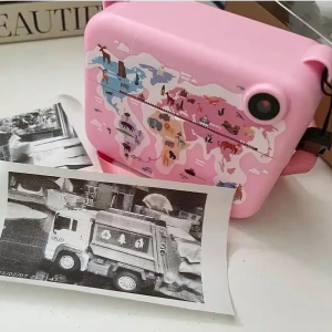 Appareil photo avec imprimante instantanée, dans sa version rose, avec une photo imprimée en noir et blanc posée devant. Cet appareil photo est posé sur une table blanche.