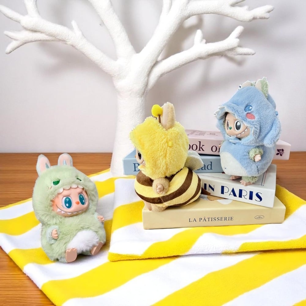 Djurdräkter till Labubu-gosedjur i teman som bi, dinosaurie och fisk, utlagda på en plan yta.