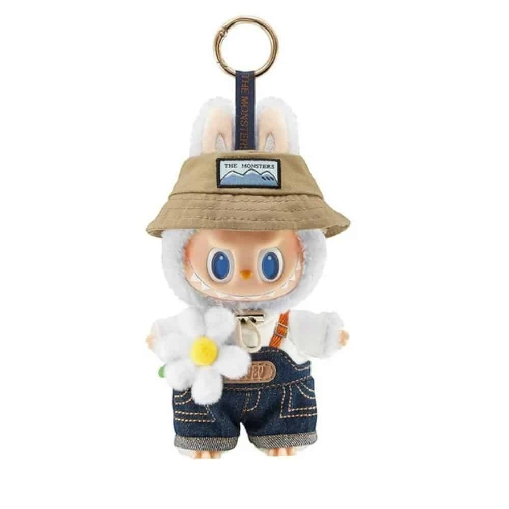 Vitt Labubu-gosedjur med beige hatt, jeanshängselbyxor och vit blomma.